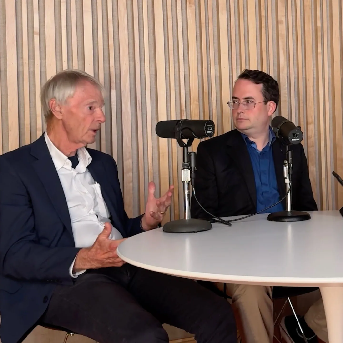 A photograph of two people talking into micphones in a podcast setting.