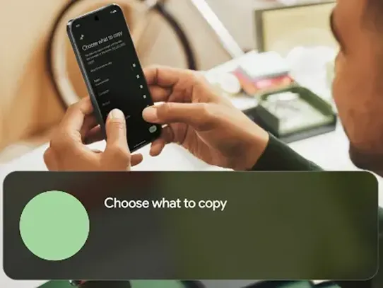 A person holds an Android phone with the screen visible. The top of the phone screen reads "Choose what to copy" with a list of options to select. There is a text overlay hovering at the bottom of the picture that reads "Choose what to copy" and the words "Photos, Apps, Music, and Contacts" cycle through.