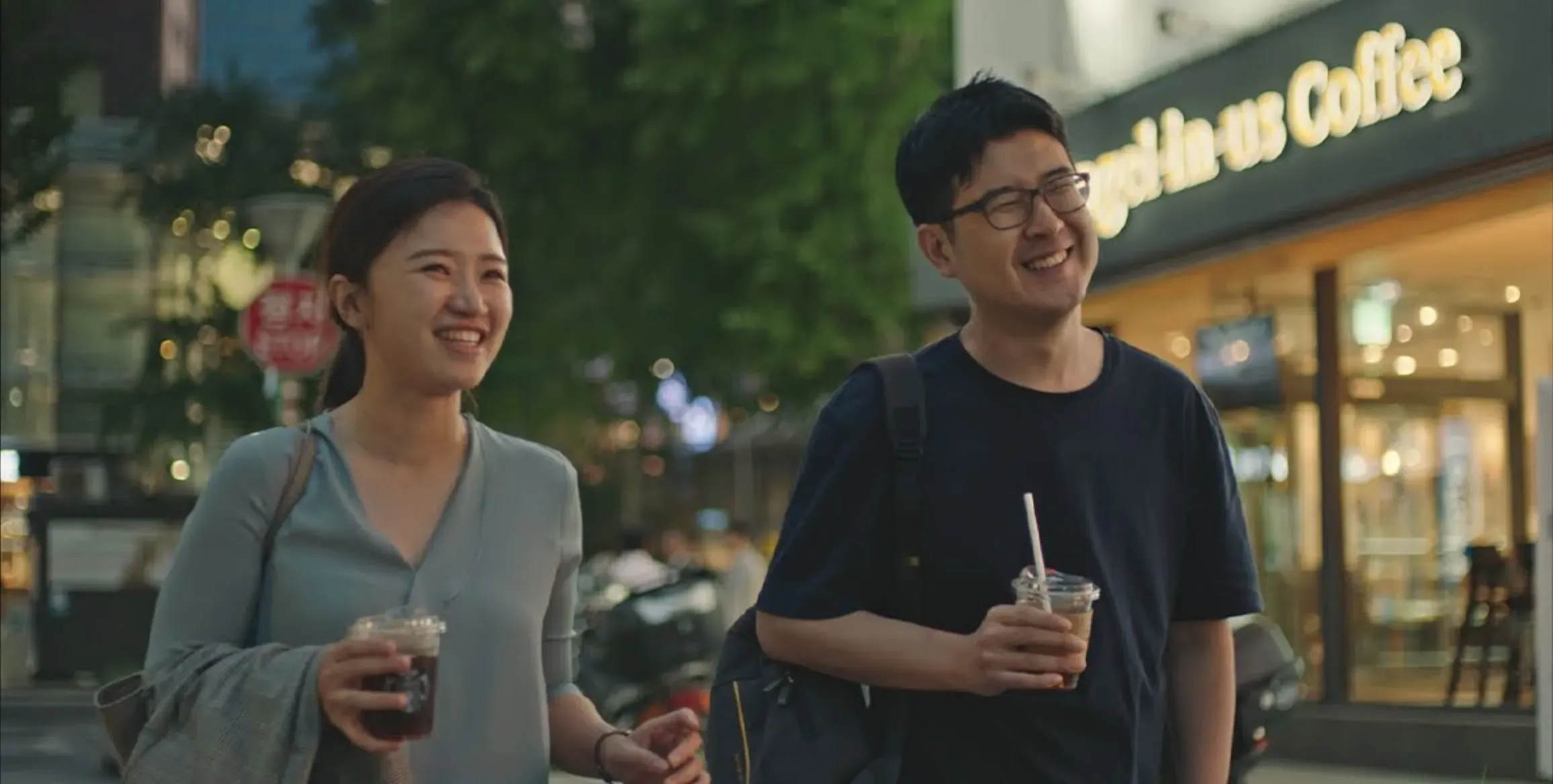 Founders, Suji and Han, are walking with drinks in their hands along a dimly lit sidewalk.