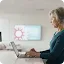 A senior woman with grey hair focused on working on her laptop at a white desk in a bright, professional office environment.