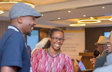A woman wearing glasses smiles pleasantly while standing with a group of people.
