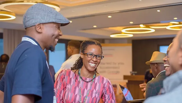 A woman wearing glasses smiles pleasantly while standing with a group of people.