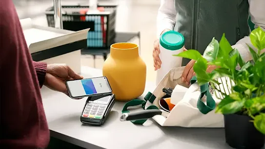 A person using a smartphone to make a Tap and Pay contactless payment at the checkout counter.
