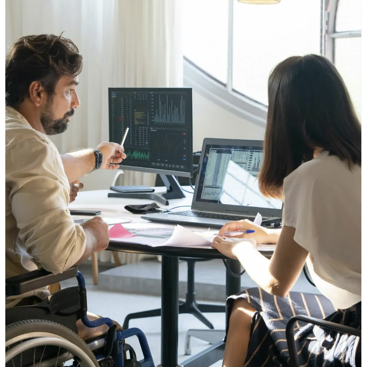 Two people are sitting at a desk discussing something on a computer screen