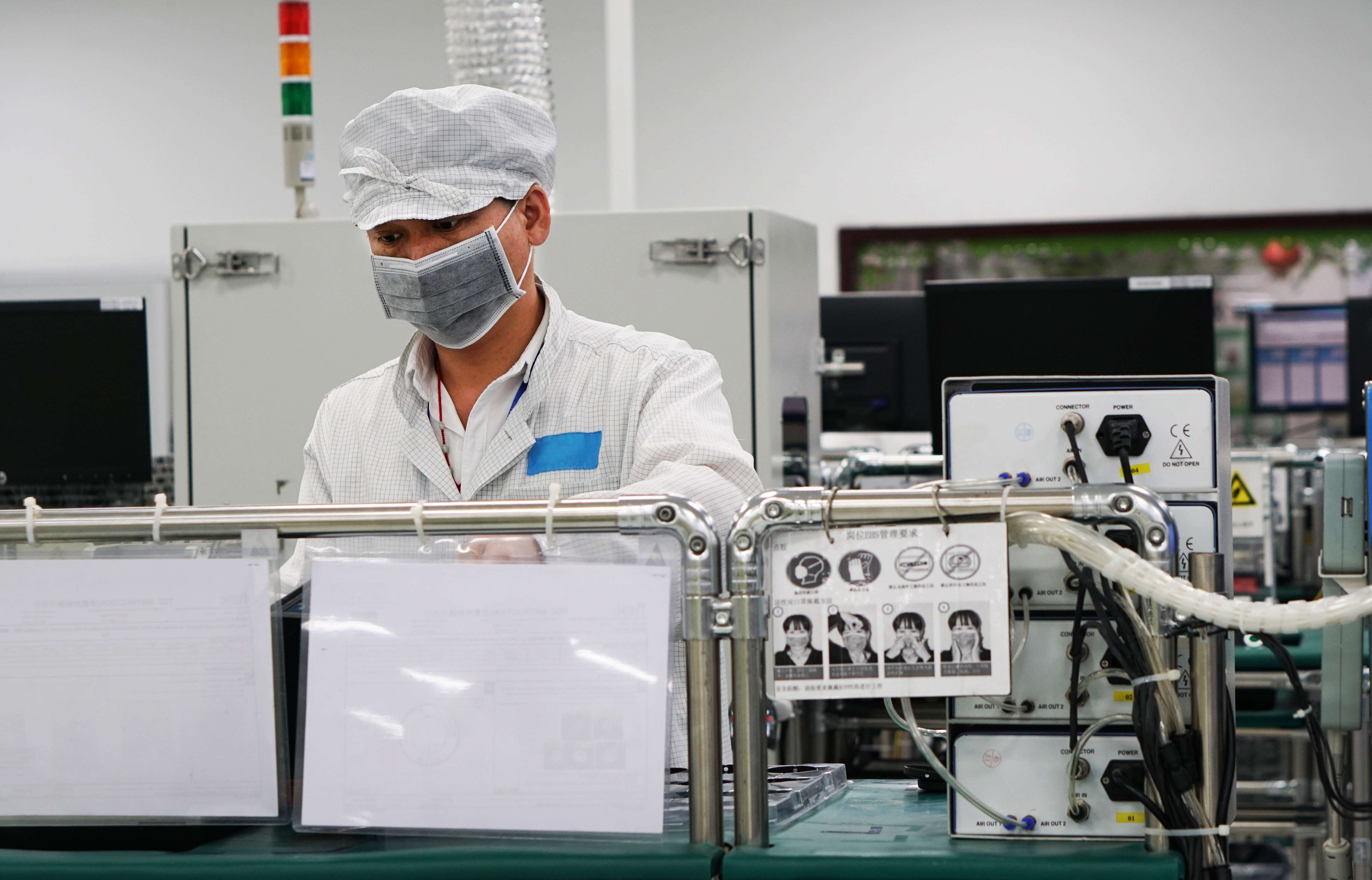 A factory worker at their station wearing a cap and mask.
