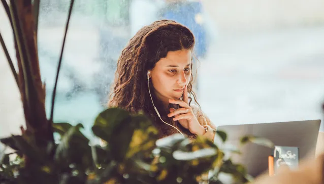 Una mujer con auriculares de cable mirando la pantalla de su portátil.