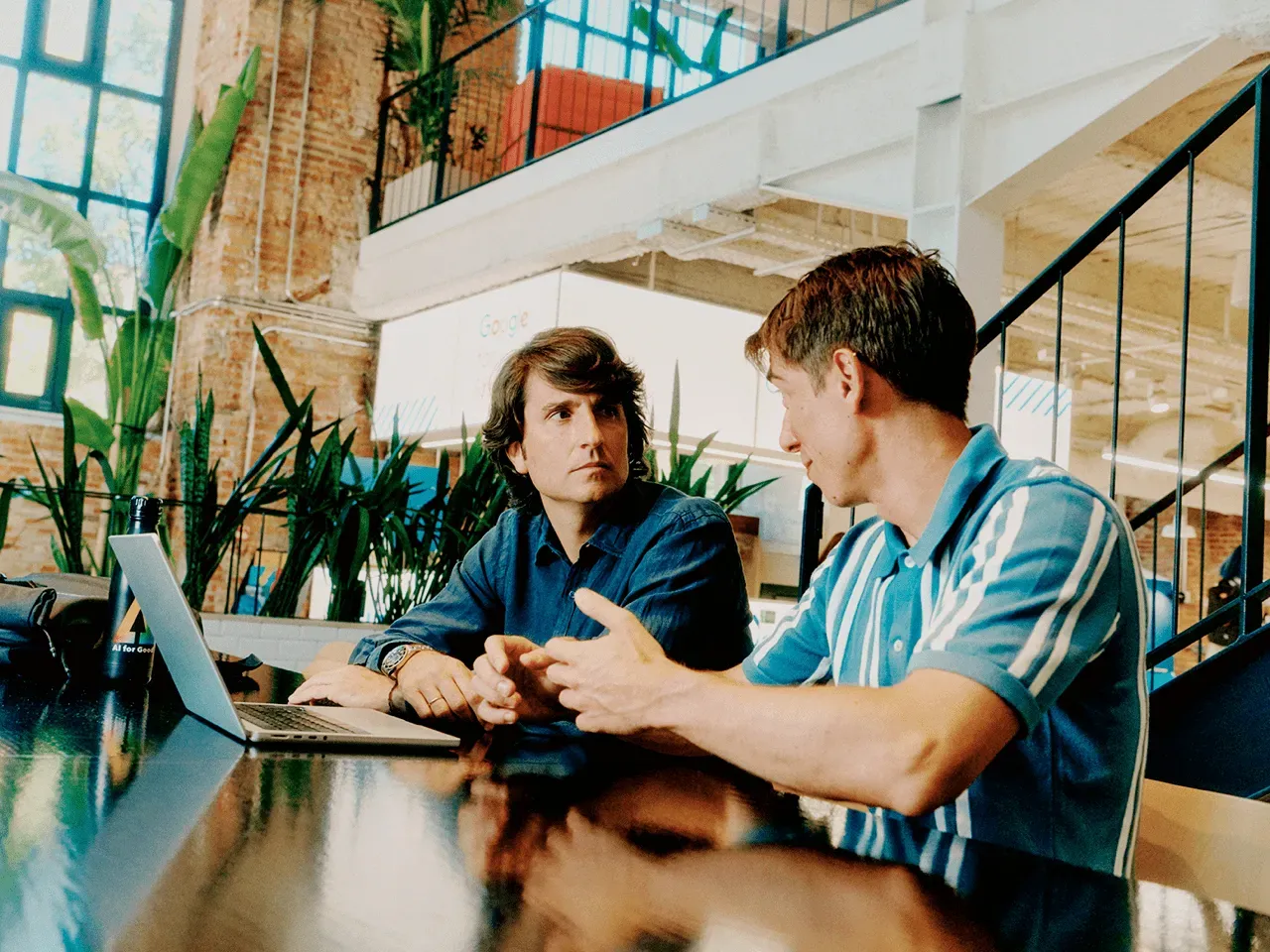 Carlos Nueno and Nacho Medrano sitting at a desk with an open laptop, having a collaborative discussion about AI health technology in a bright, modern office setting.