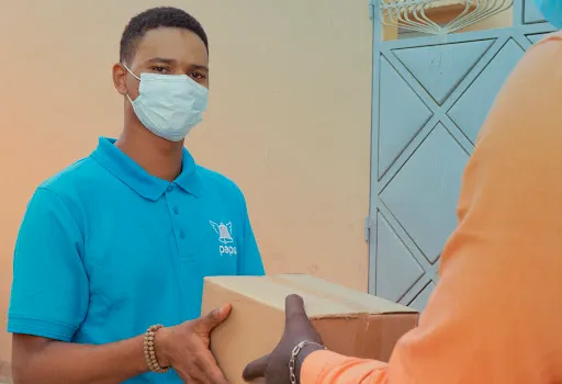A Paps delivery person wearing a mask delivers a package to a customer.