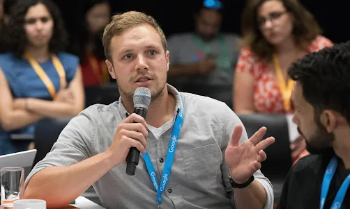 Seated at a table, a Google-tagged attendee is speaking to the host.