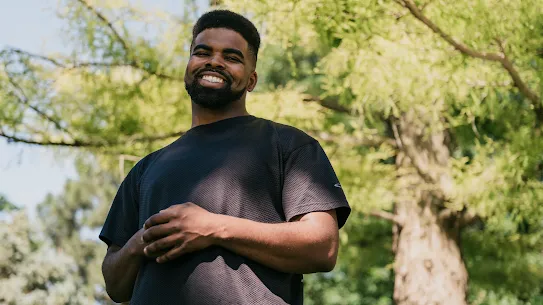 A recent Google Skilled Trades and Readiness Program graduate stands outside under the trees, smiling.