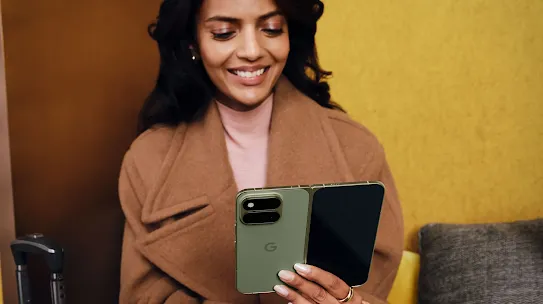 A woman smiling while holding an open olive green Google Pixel Fold phone.
