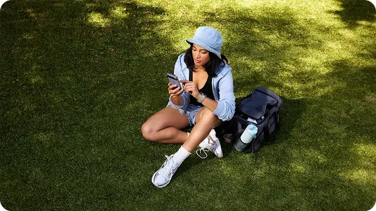 Woman using her phone while outside, in a field or park.