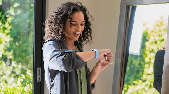 A woman is smiling while looking at her smartwatch.