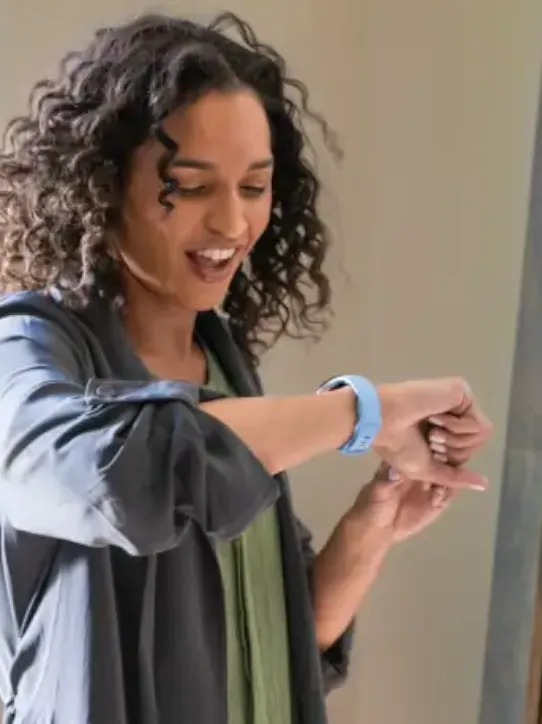 A woman is smiling while looking at her smartwatch.