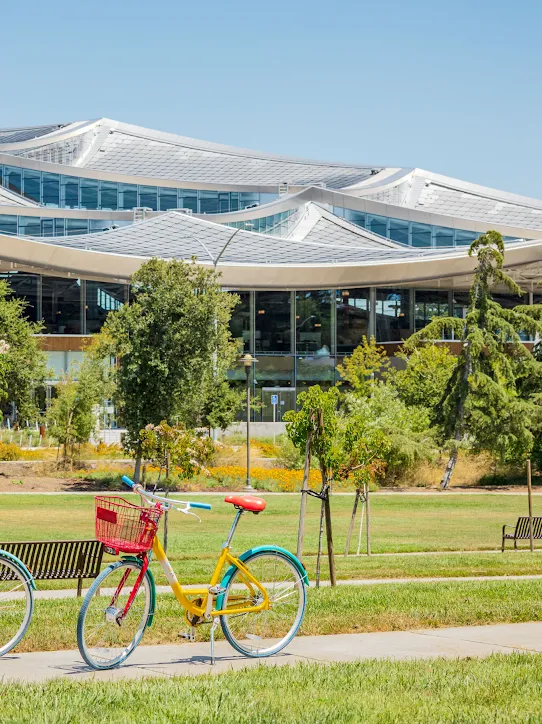 A yellow, green, blue and red gBike sitting in front of a silver-colored building on the Google Bay View campus.