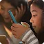 A close-up, warm-toned photograph of two young people looking at the screens of their smartphones in a focused manner.