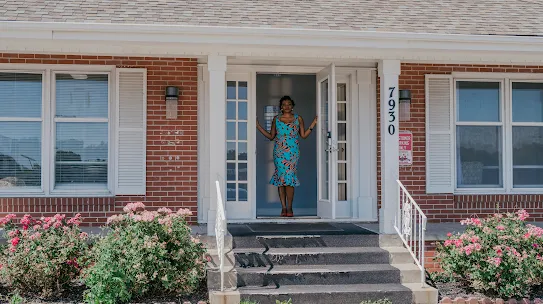 Karine Sokopoh stands in the doorway of a brick building on a sunny afternoon
