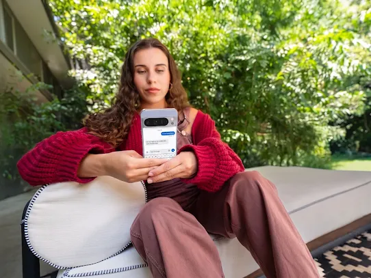 Une femme utilise son téléphone à l'extérieur, avec des arbres en arrière-plan.