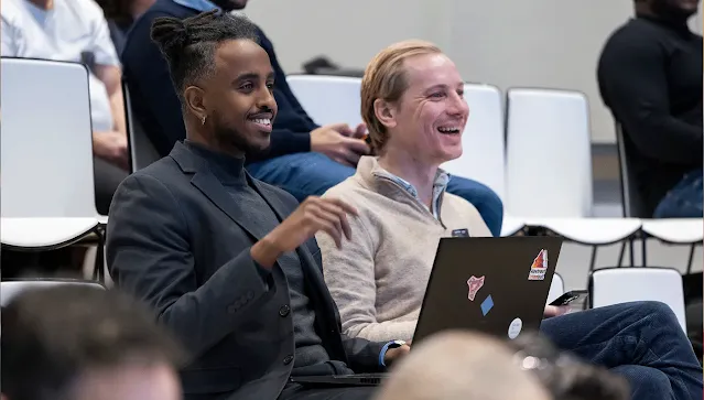 One person in the audience, with a laptop in front, is talking and smiling at the host.