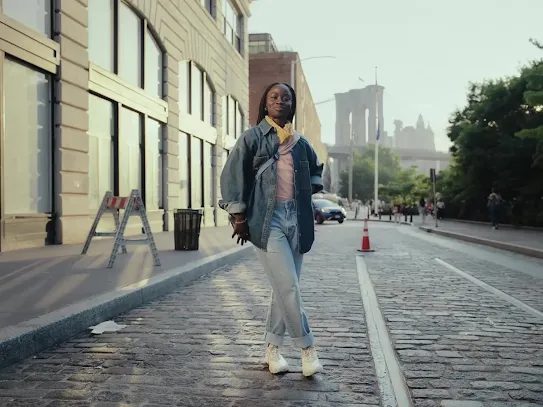 Someone getting their picture taken on the street in front of a building is used as an example of how Magic Eraser works.  
