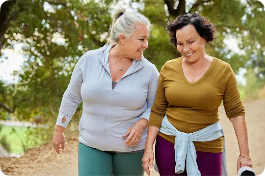 Two older women smiling and walking together on an outdoor trail.
