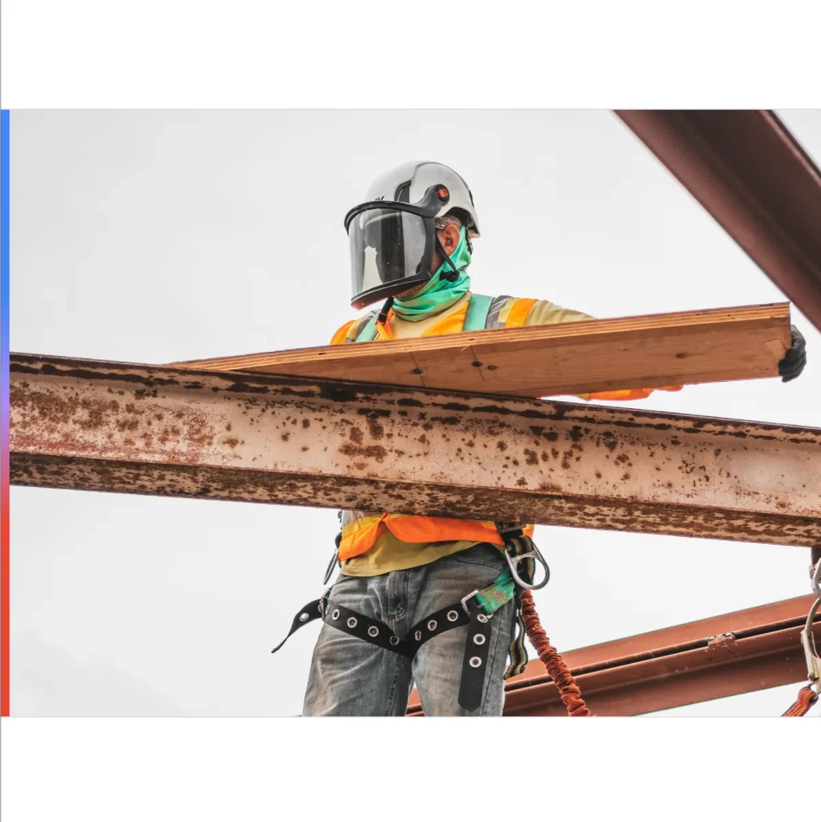 An electrician in a helmet and face shield rests a wooden beam on top of a metal beam