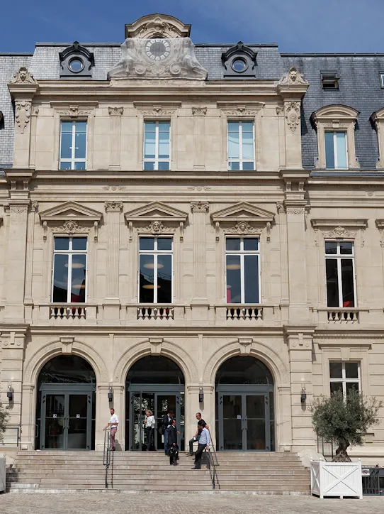 A small group of people talk on the steps of a tan-colored building.