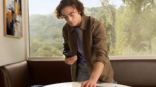 Man using an Android phone. He is standing over a desk with several documents and notepads and is pointing the device