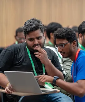 A man in blue shirt showing something one a laptop to another man.