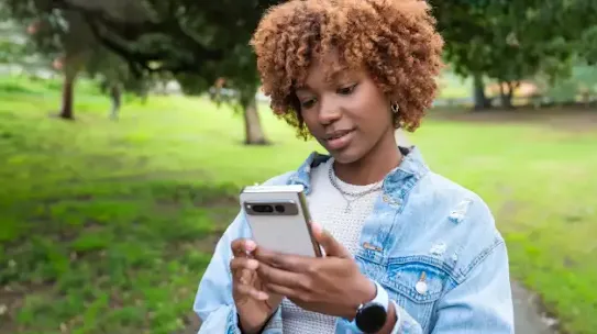 A woman in a park holding a smartphone.