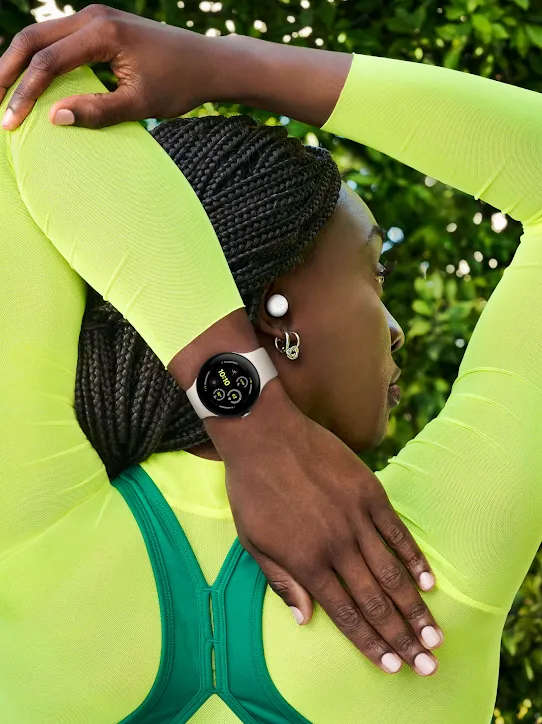 Eine Person in einem neongelben Oberteil, die Pixel Buds und eine Pixel Watch trägt, dehnt ihren linken Arm hinter dem Kopf.