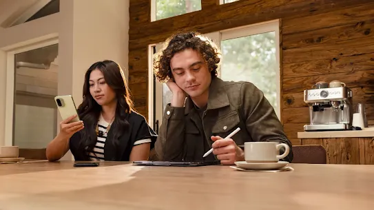A woman is checking her Android phone. She is sitting next to a man who has a cup of coffee in front of him.