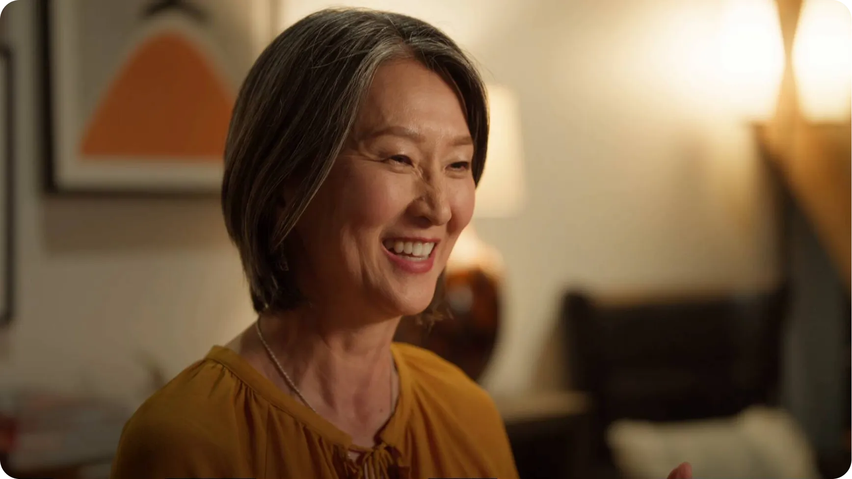 A person sits and smiles in a warmly lit room.