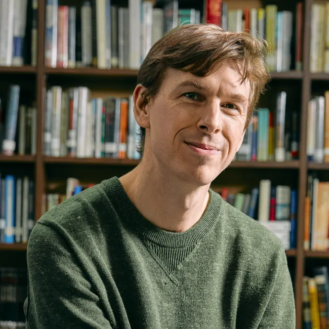 A man with brown hair wearing a green sweater smiling at the camera
