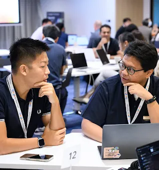 Two men wearing Google for Startups lanyards discussing work at a laptop during a workshop.