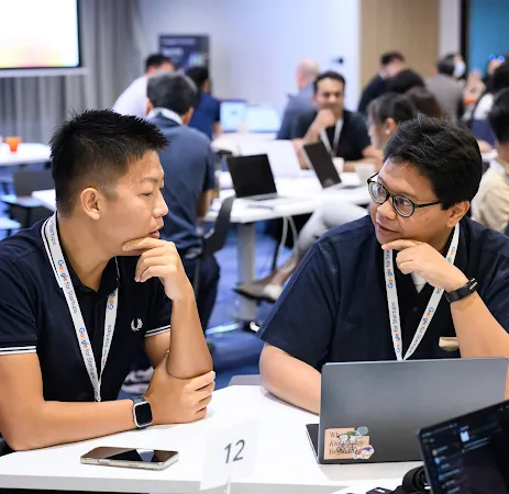 Two men wearing Google for Startups lanyards discussing work at a laptop during a workshop.