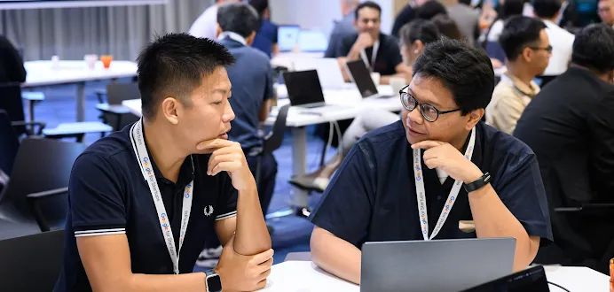 Two men wearing Google for Startups lanyards discussing work at a laptop during a workshop.