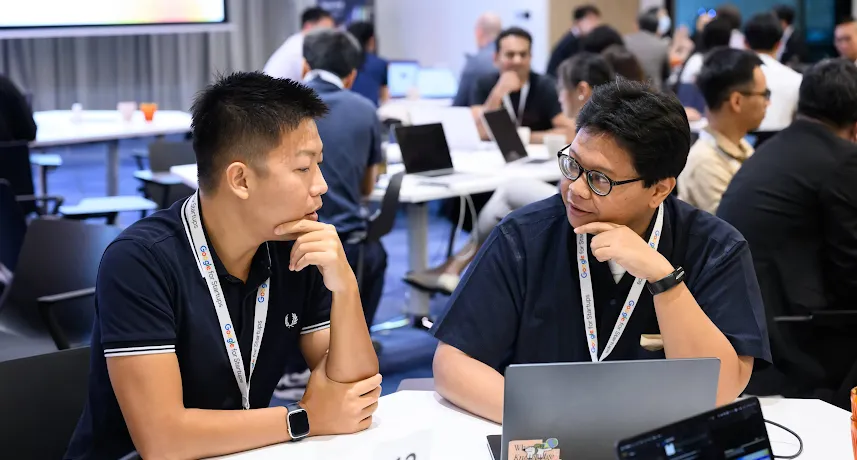 Two men wearing Google for Startups lanyards discussing work at a laptop during a workshop.