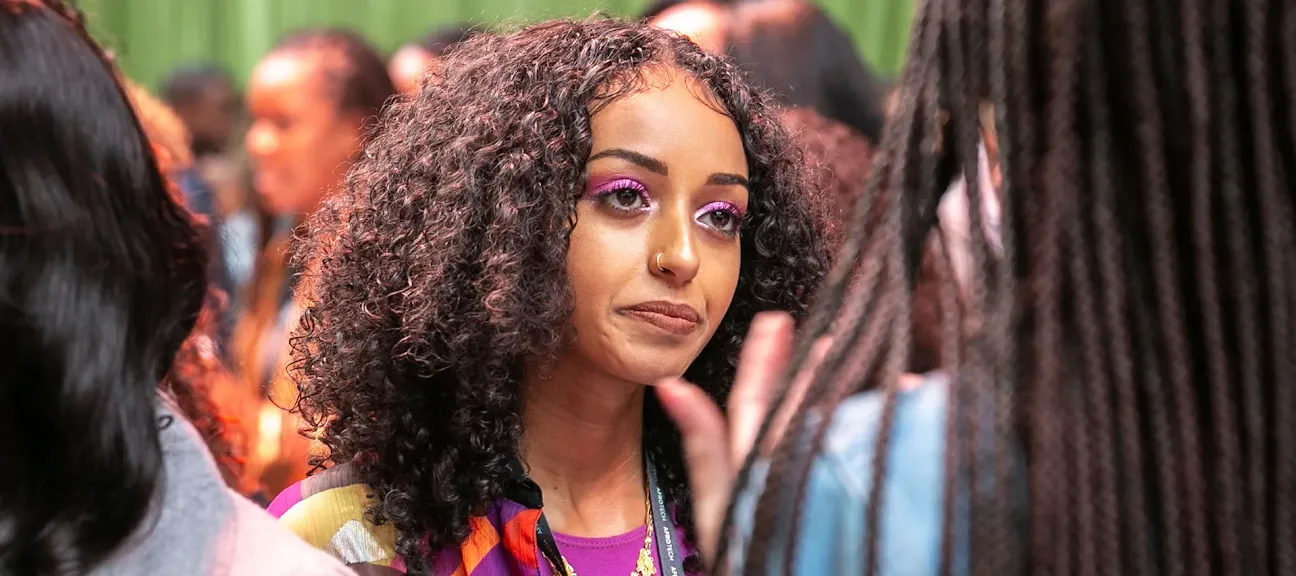 A woman with curly hair is listening to other woman in crowd