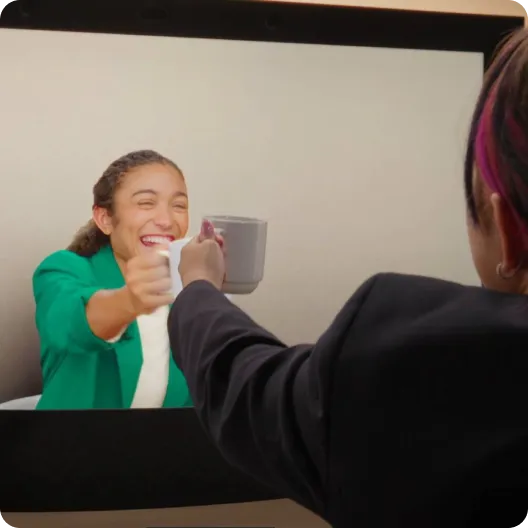 Colleagues toast toward the screen with coffee mugs during a Google Beam video meeting.