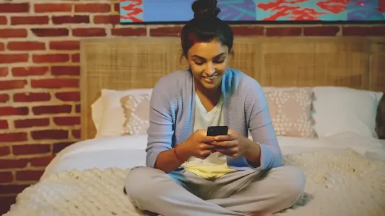 Woman sitting on bed with Android phone