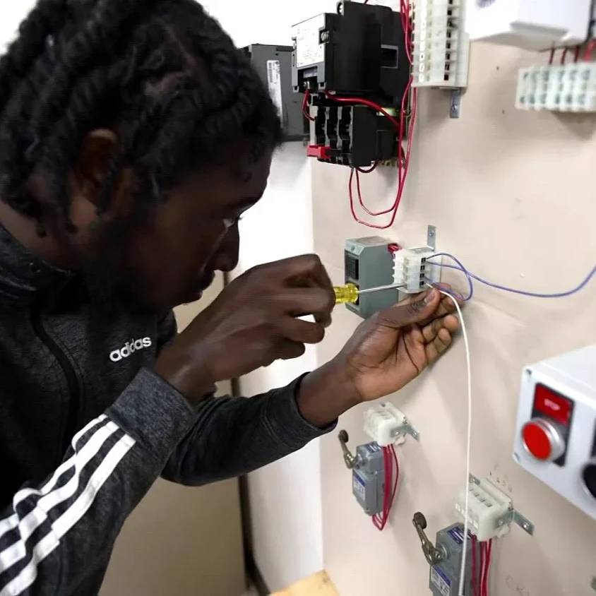 An electrician with a screwdriver concenrates on a wall mounted circuit