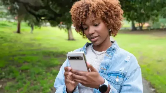 A woman in a park holding a smartphone.