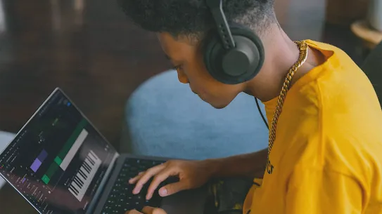 Young man in yellow shirt producing music on laptop.