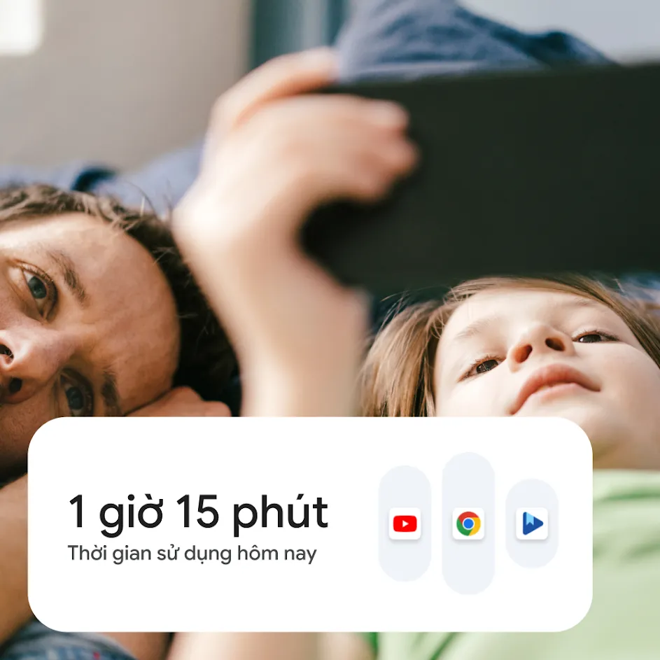 Ảnh chụp một người cha đang cùng con trai nằm ở nhà và xem nội dung trên điện thoại thông minh với nét mặt vui vẻ. Ở góc trên bên trái của bức ảnh có biểu tượng hồ sơ người dùng của cậu bé. Ở góc dưới cùng bên trái của bức ảnh có giao diện người dùng cho chế độ cài đặt thời gian sử dụng thiết bị. 