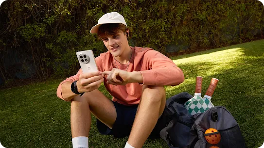 A young man using an Android phone on a grassy field.