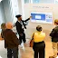 A presenter pointing at a large digital screen titled "Learning through video" while an audience watches in a bright office space.