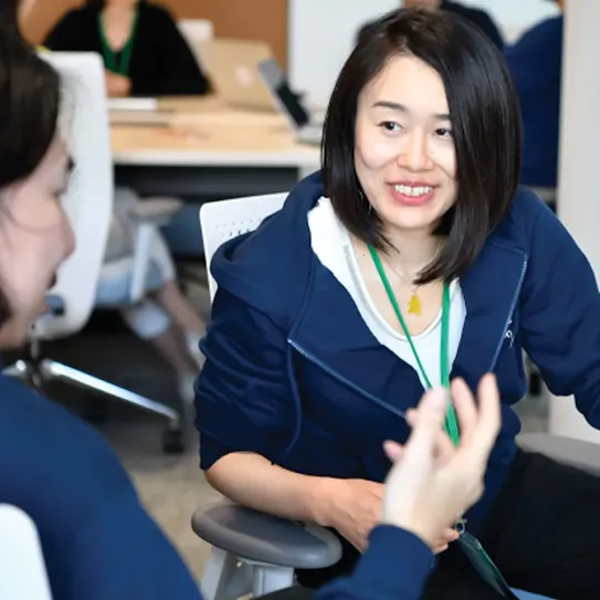 A woman in focus is smiling at other woman while sitting on chair