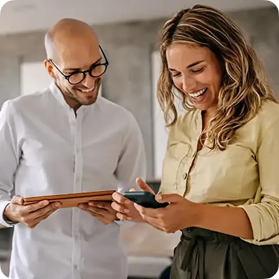 Two work collegues reviewing information on a tablet and mobile device at the office.