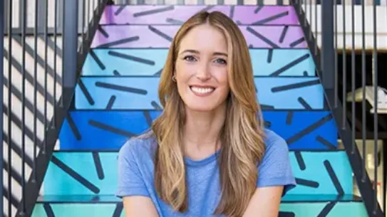Founder Andrea Barber smiles in front of a colorful staricase